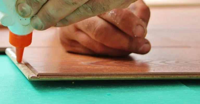 Close-up of a glue bottle nozzle laying a bead of adhesive along the edge of a wooden board