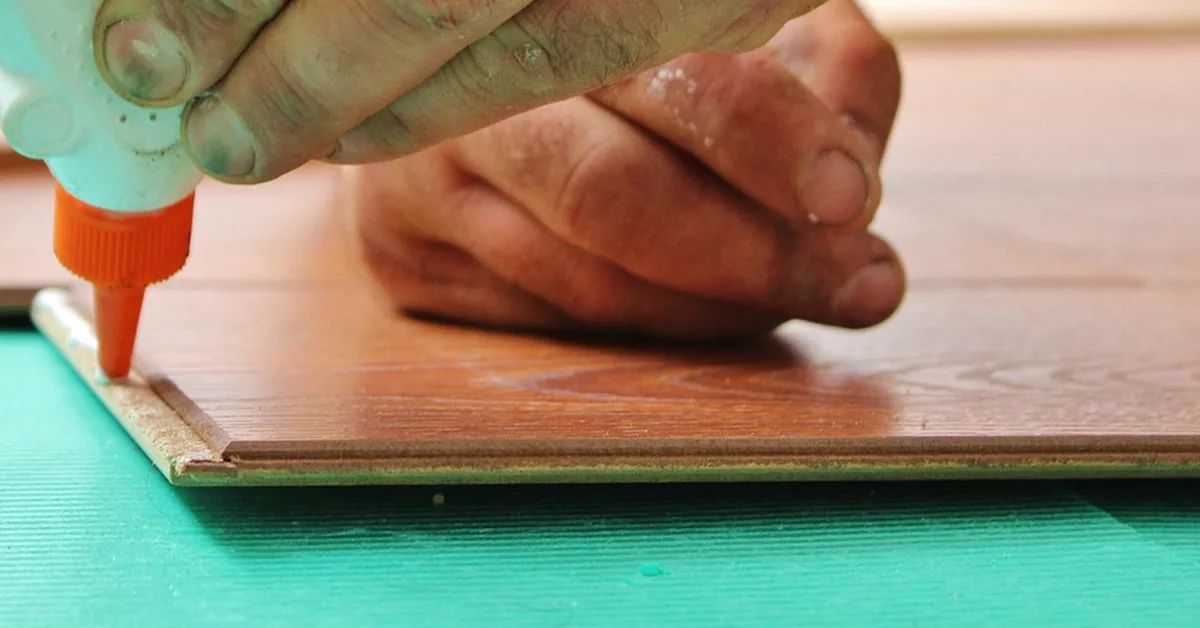 Close-up of a glue bottle nozzle laying a bead of adhesive along the edge of a wooden board
