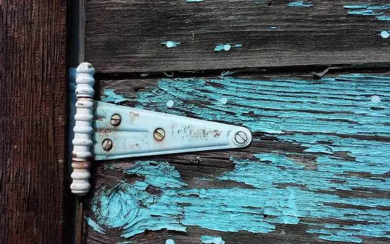Old metal door hinge surrounded by peeling turquoise paint on wood