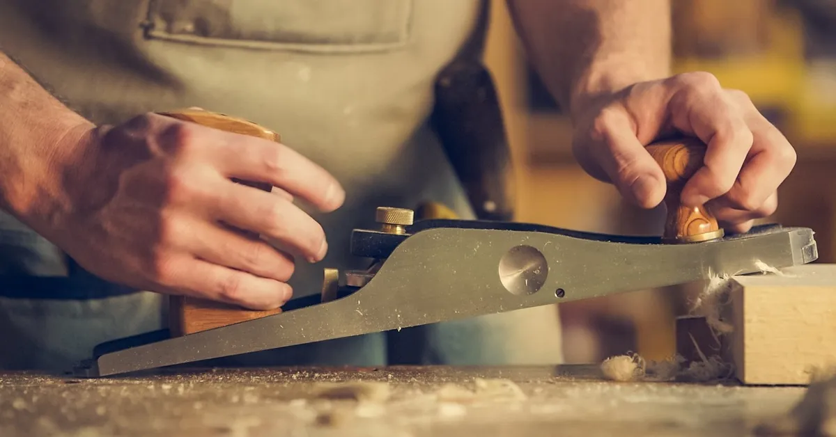Woodworker smoothing a board with a hand plane at a workbench