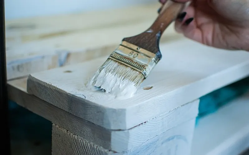 Brushing white primer onto a sanded wood surface during refinishing