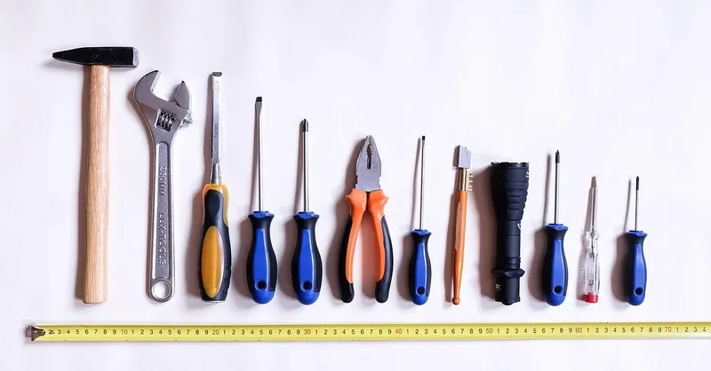 Hammer, screwdrivers, pliers and tape measure laid out for a wood repair job