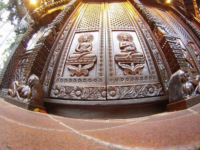 Ornately carved dark wood temple double door featuring seated Buddha relief panels