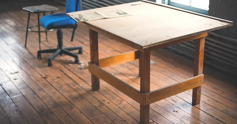 Wooden workshop table with solid wood legs and a plywood top beside an office chair