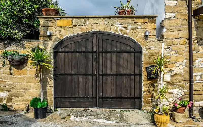 Arched teak-toned double door built into a stone garden wall entrance