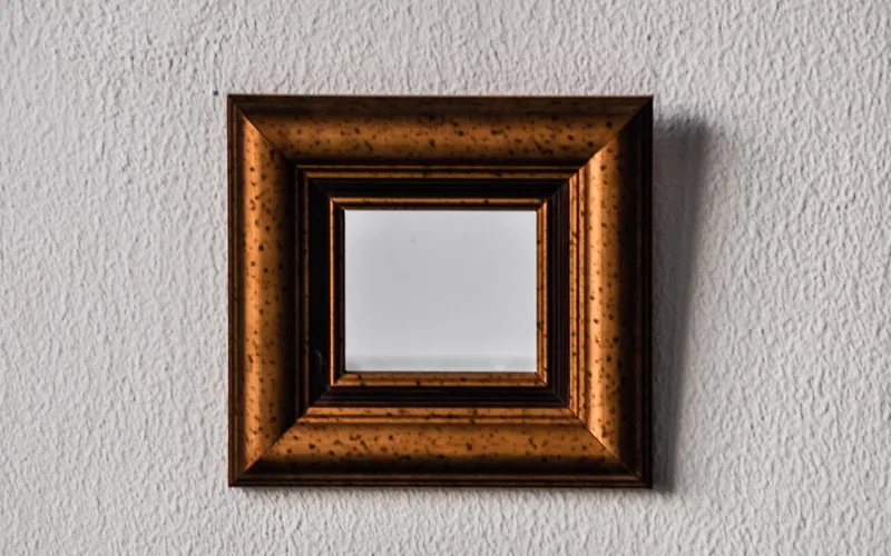 Ornately carved wood-framed mirror mounted on a textured wall Ornately carved wood-framed mirror mounted on a textured wall