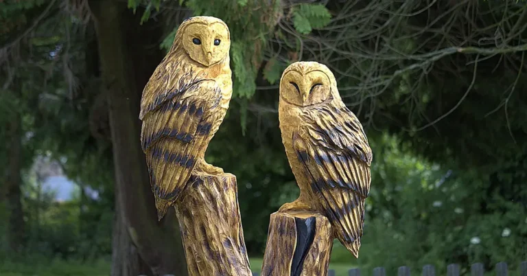 Two chainsaw-carved owls perched on weathered tree stump pillars in a garden