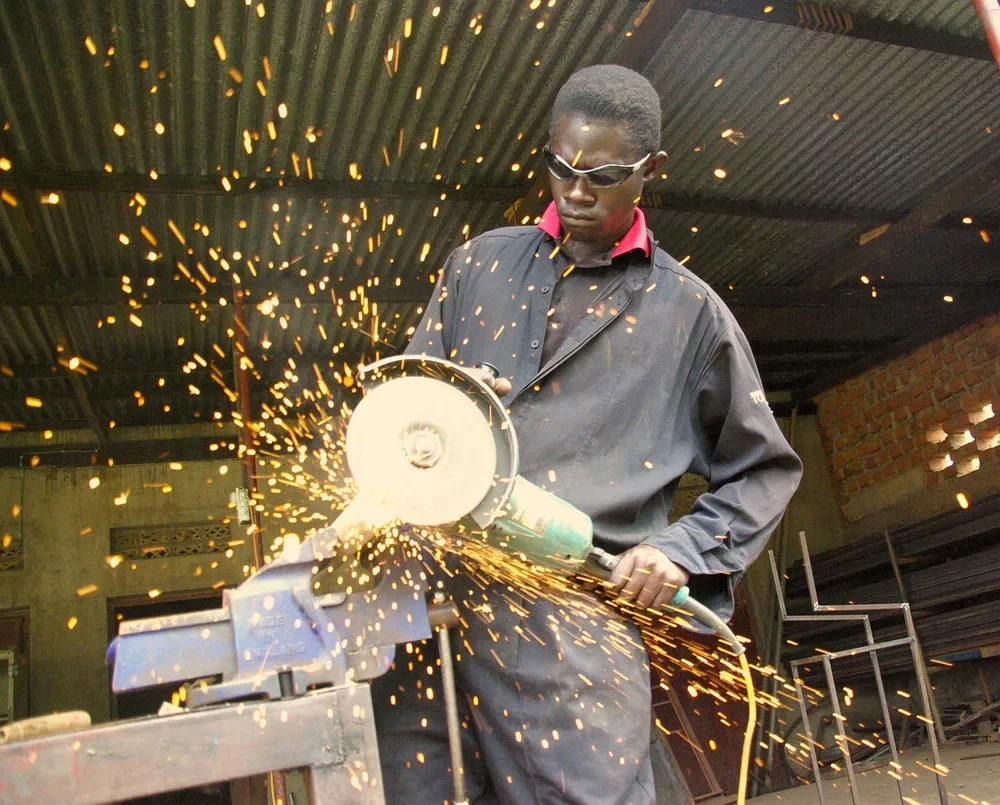 Worker in safety glasses cutting steel with an angle grinder at a workbench