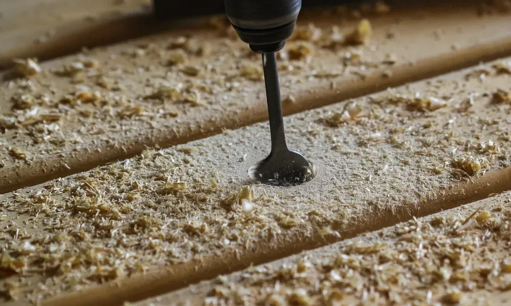 Drill bit boring into a wood board with sawdust around the hole