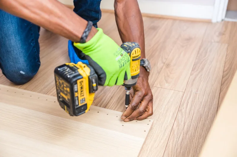 Person driving screws into a pre-drilled flat-pack panel with a cordless drill Person driving screws into a pre-drilled flat-pack panel with a cordless drill