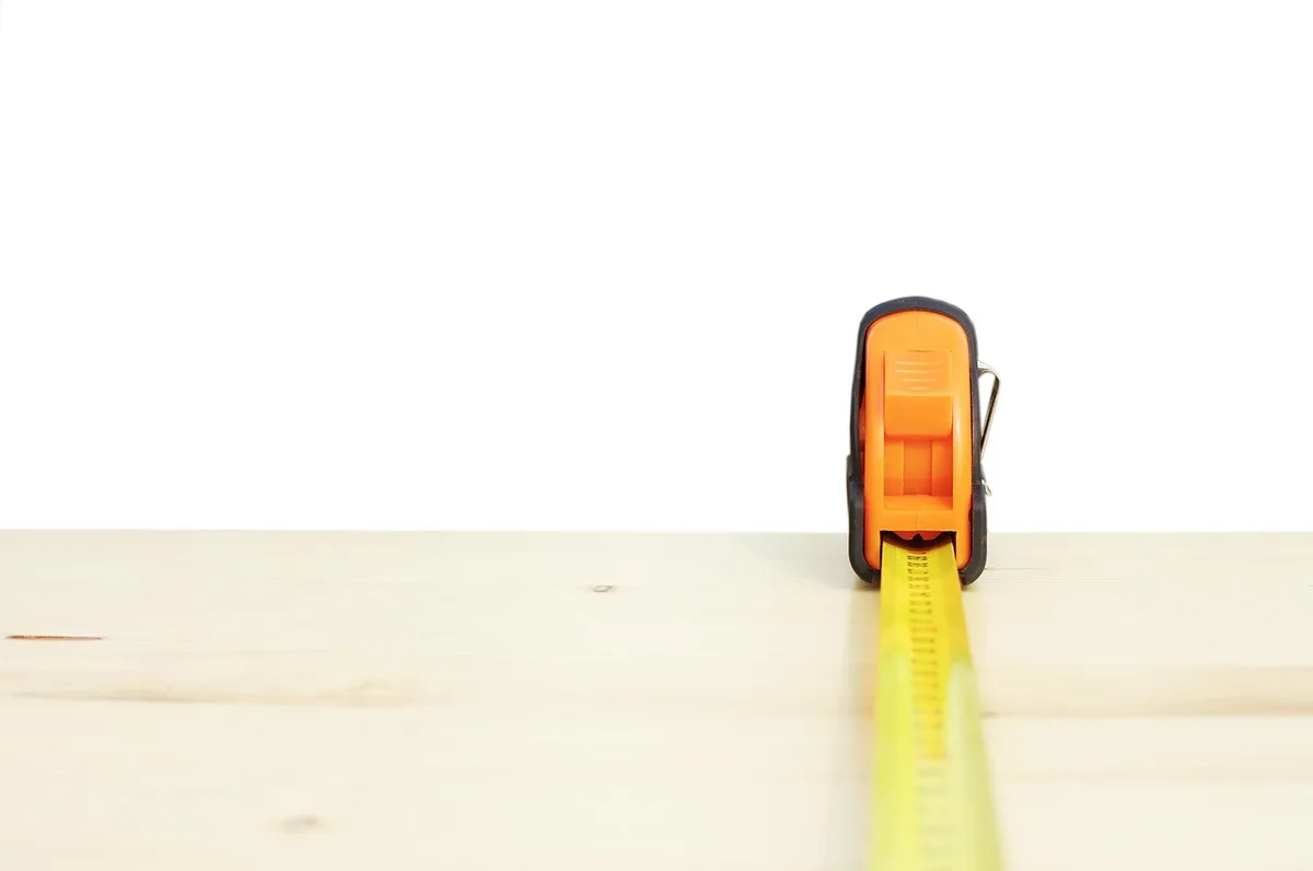 Tape measure extended across a wood board to measure length