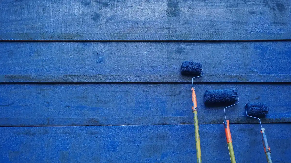 Paint rollers leaning against a painted wood panel showing even roller application