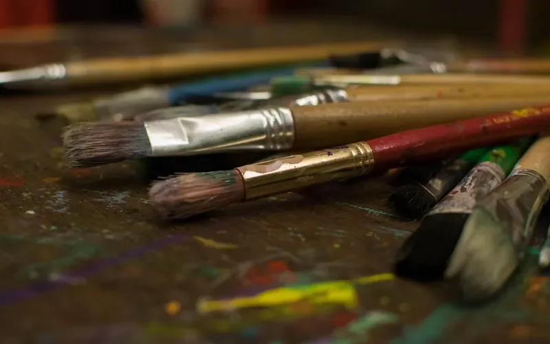 Well-used flat paintbrushes lying on a paint-stained craft table
