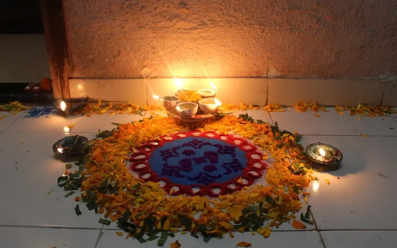 Floor rangoli lit by small oil lamps on a tiled entrance