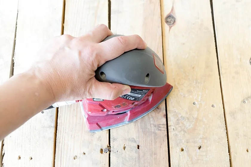 Hand sanding a wood board surface with an orbital sander during repair