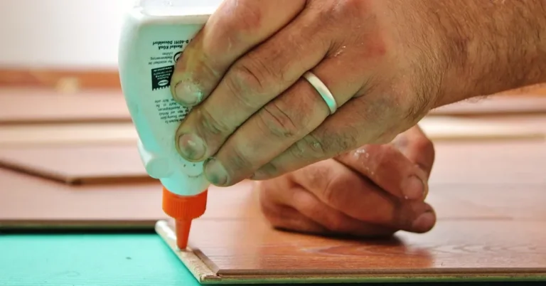 Hand squeezing wood glue from a bottle along the edge of a board before a glue-up