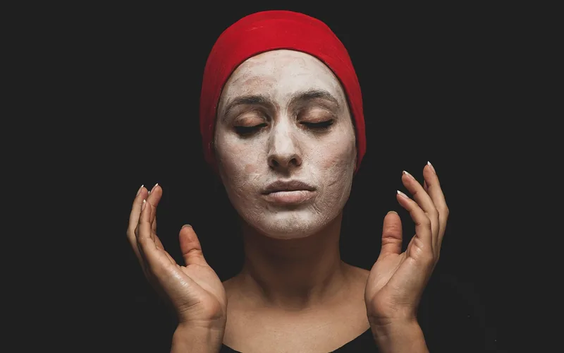 woman with a natural clay face mask applied, eyes closed, hands raised near her face