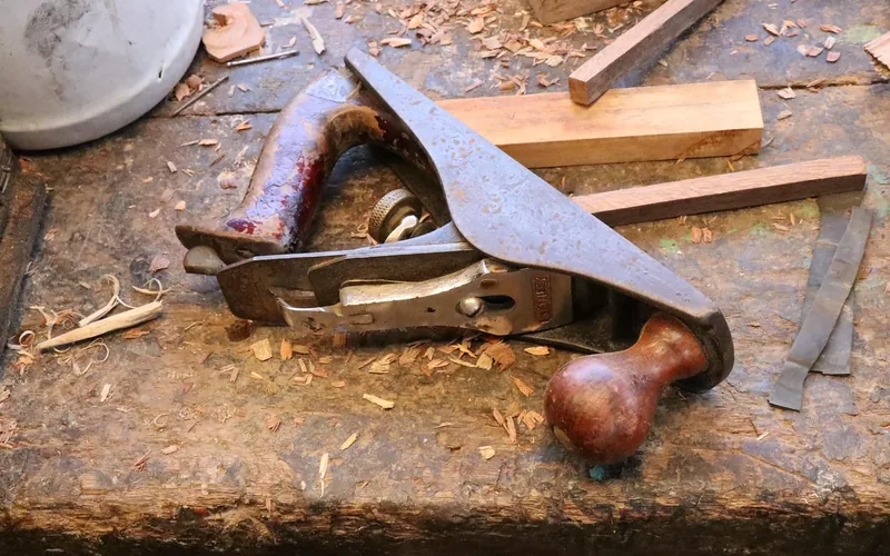 Hand plane and wood shavings on a workshop bench set up before stripping an old finish