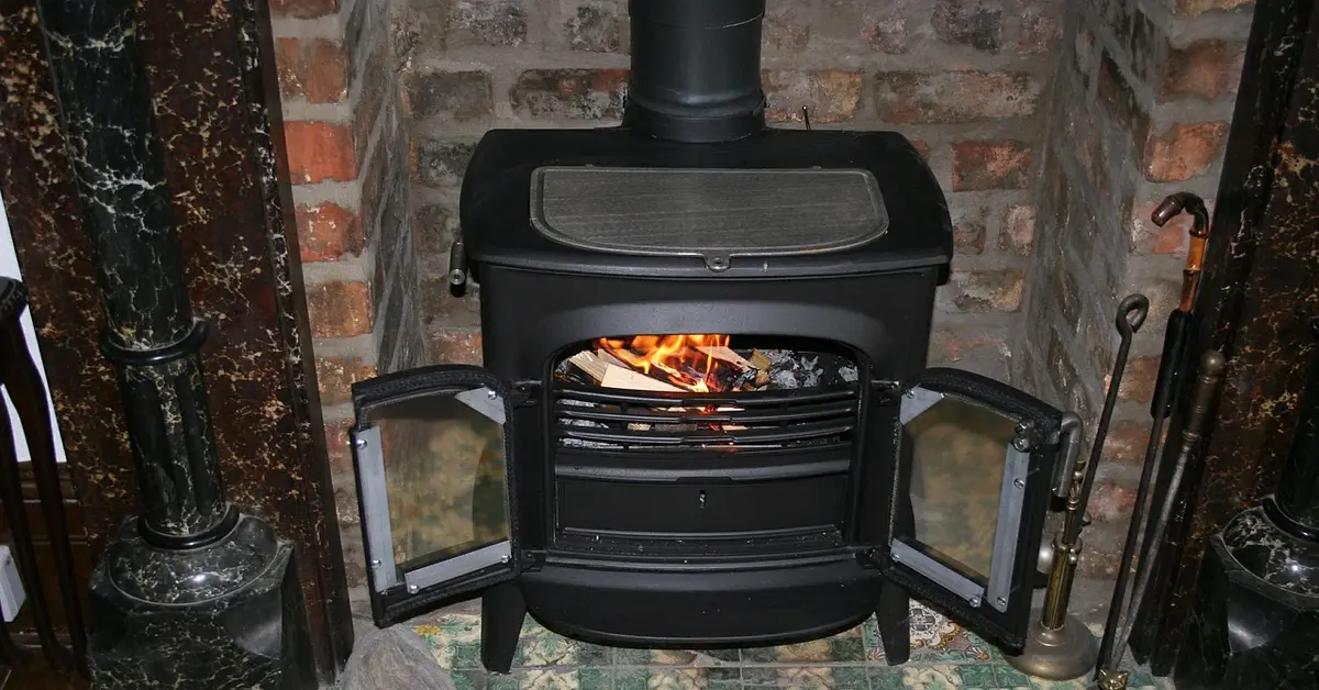 Cast iron wood stove with open doors burning in a brick fireplace, similar to All Nighter models