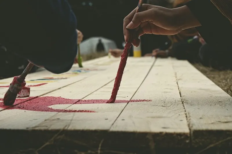 Hand applying colored exterior wood stain to a wood board with a brush
