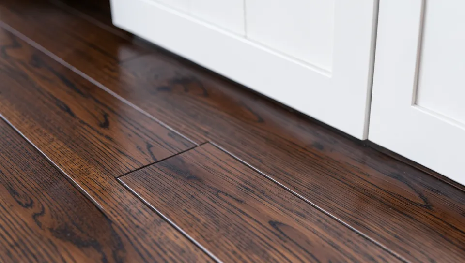 close up of dark walnut hardwood flooring boards next to a white kitchen cabinet base