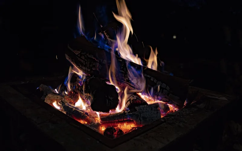 Black steel wood-burning fire pit glowing with orange flames in a backyard at night Black steel wood-burning fire pit glowing with orange flames in a backyard at night
