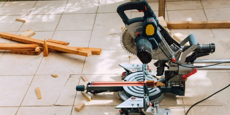 Cordless miter saw being used outdoors on a patio job site with cut lumber scraps nearby