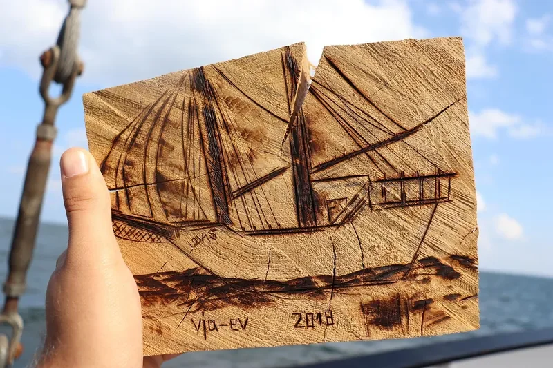 End-grain log slice carved with a sailing ship design, held up against the sea