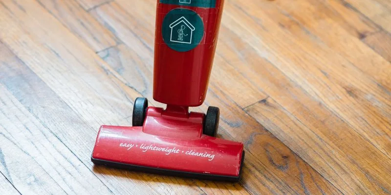 red electric broom style stick vacuum on a hardwood floor