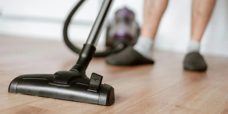 vacuuming a hardwood floor with a canister vacuum hose attachment