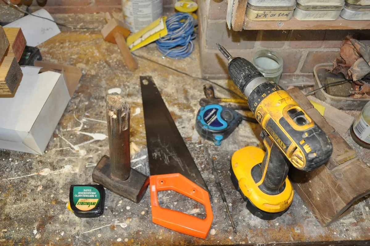 Handsaw, cordless drill and tape measures on a sawdust-covered workbench