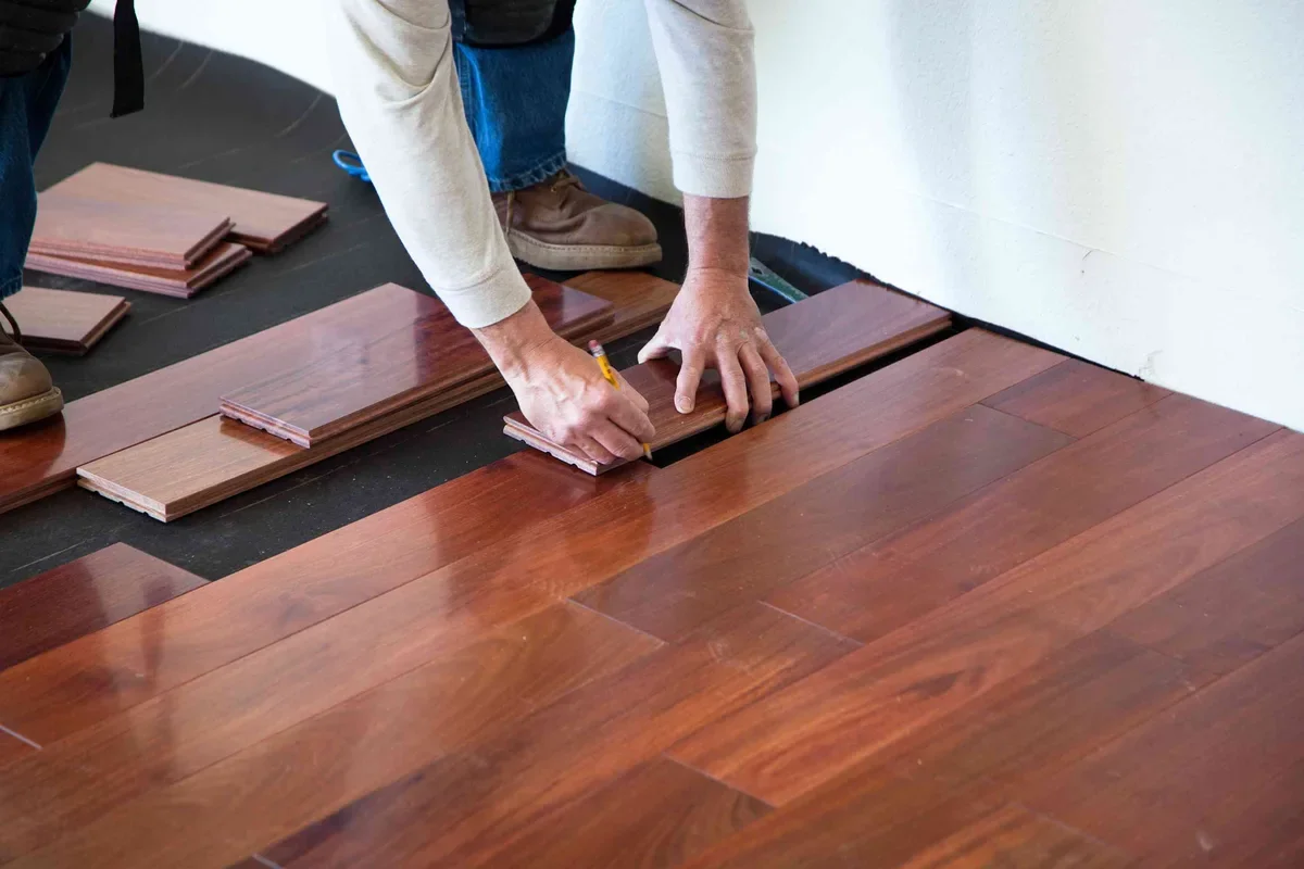 Installer fitting dark stained hardwood floor planks into place with pencil marking