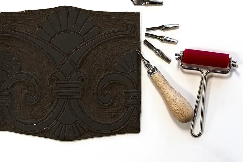 Carved relief printing block with V-shaped gouges and a red brayer roller beside it