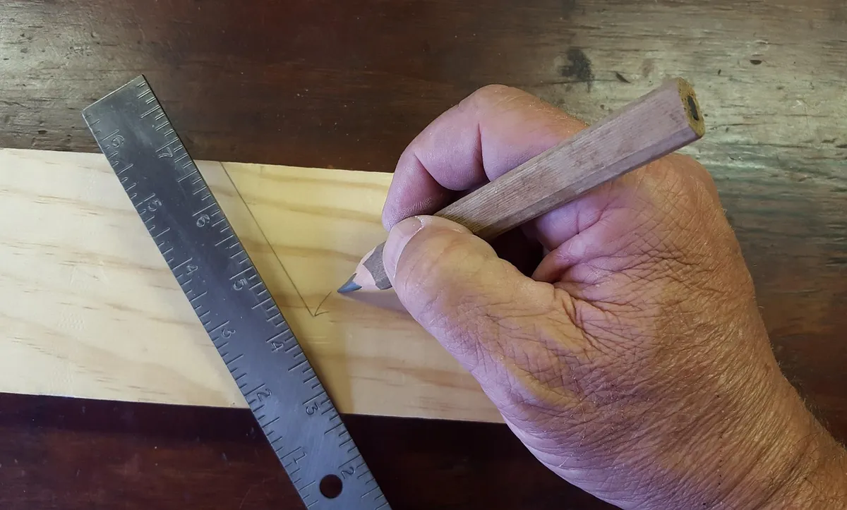 Hand marking a cut line on a pine board with a steel ruler and pencil