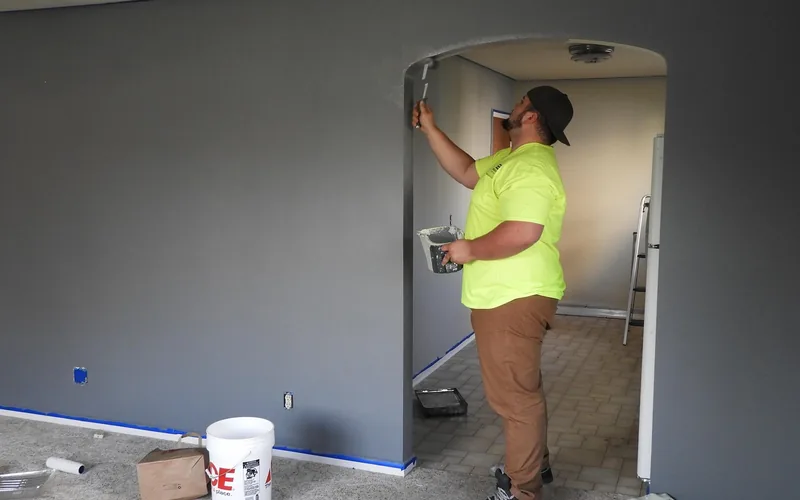 painter rolling interior wall paint onto a living room wall indoors
