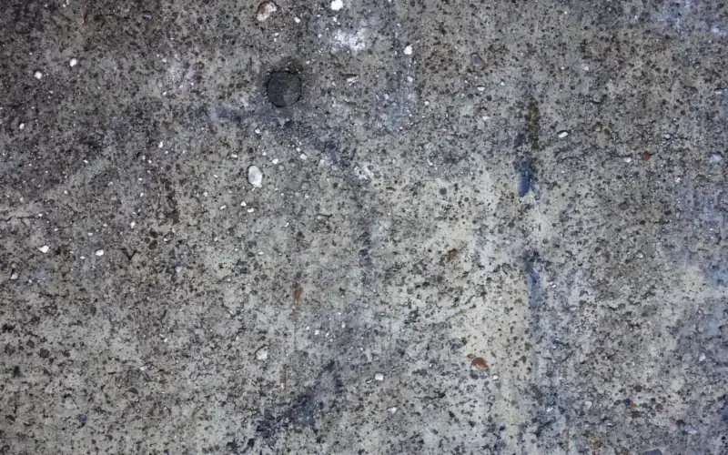 Close-up of a pitted gray concrete wall surface with small pores and pits