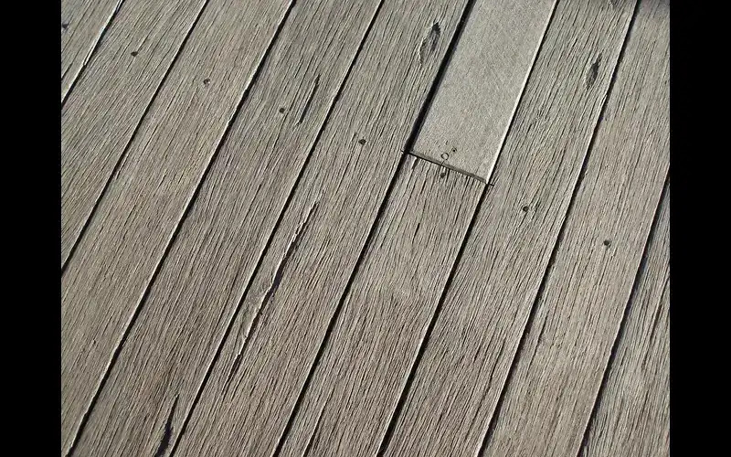 Weathered gray wooden deck boards that need cleaning and a dryness check before painting