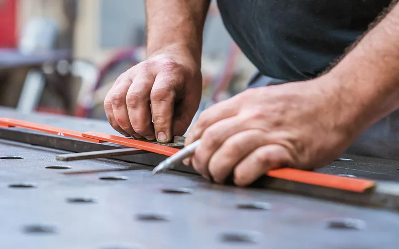 Hands measuring and marking with a steel rule and scribe on a metal work surface Hands measuring and marking with a steel rule and scribe on a metal work surface