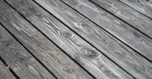 Weathered gray wooden deck boards with visible grain and nail heads, ready for restaining