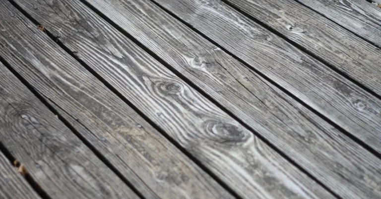 Weathered gray wooden deck boards with visible grain and nail heads, ready for restaining