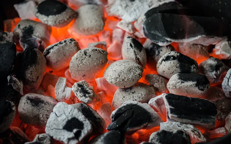 Charcoal smoker with glowing coals and rising smoke, showing the setup used to smoke meat with wood chunks