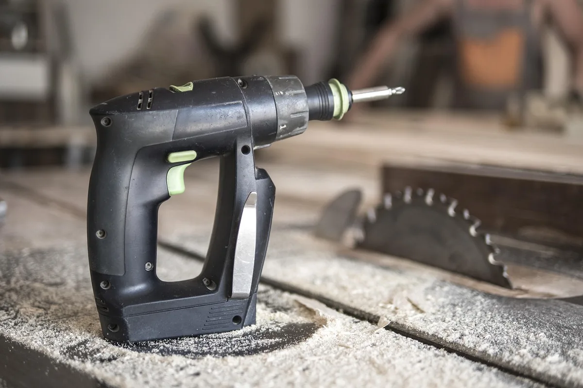 Sawdust on a steel table saw top beside the blade and a cordless drill