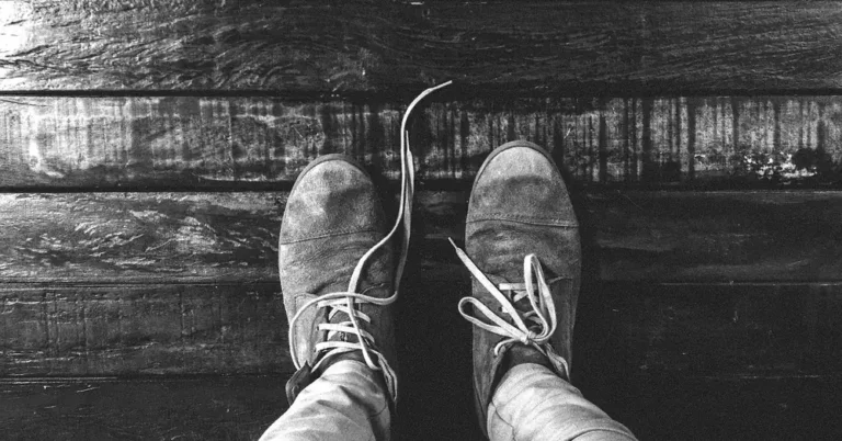 Worn sneakers standing on dark wood floor planks