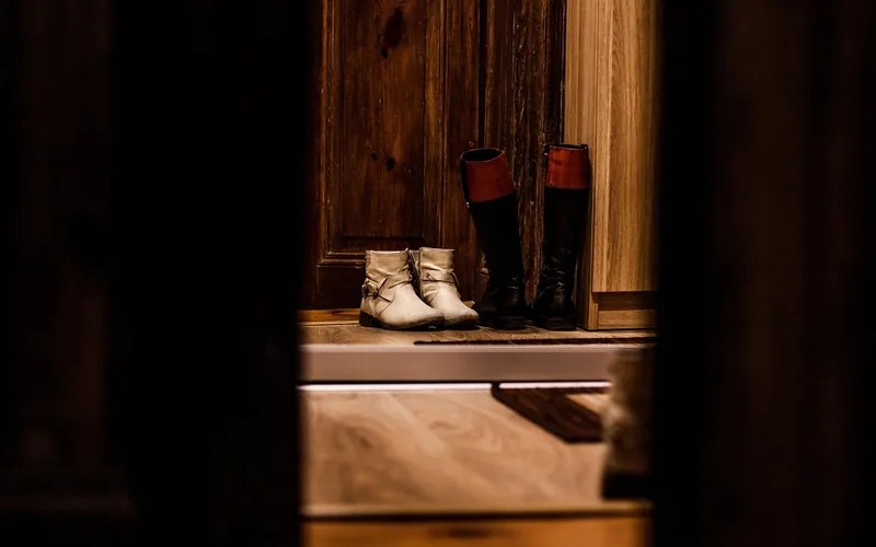Boots and shoes lined up at a doorway next to a wood floor entry