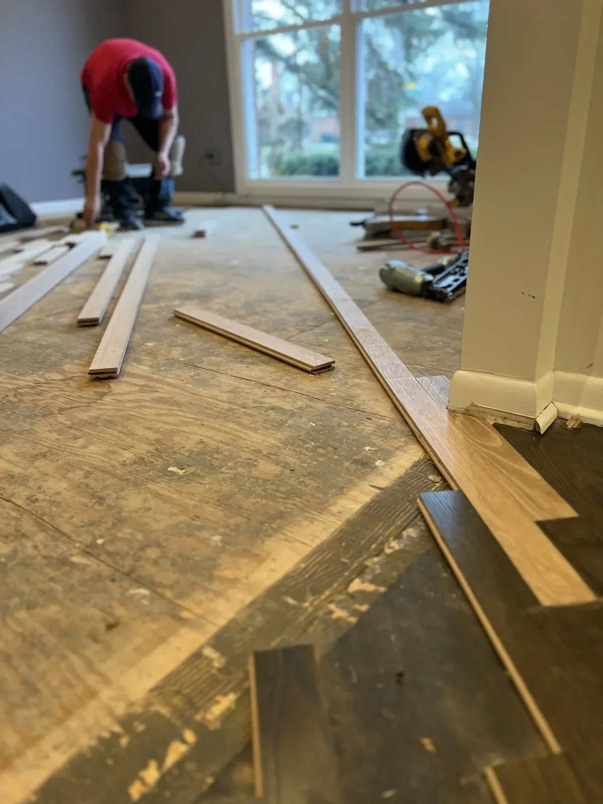 Solid hardwood plank flooring being installed over plywood subfloor near entryway
