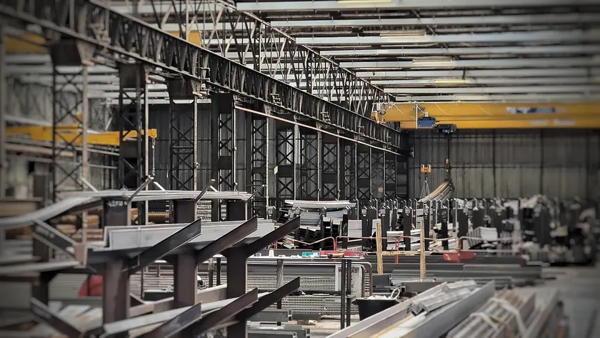 Rows of prefabricated steel beams and framing components staged in a steel fabrication warehouse