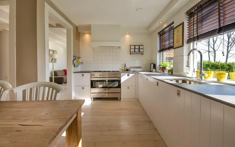 Sunlit kitchen with light plank flooring beside a large window Sunlit kitchen with light plank flooring beside a large window
