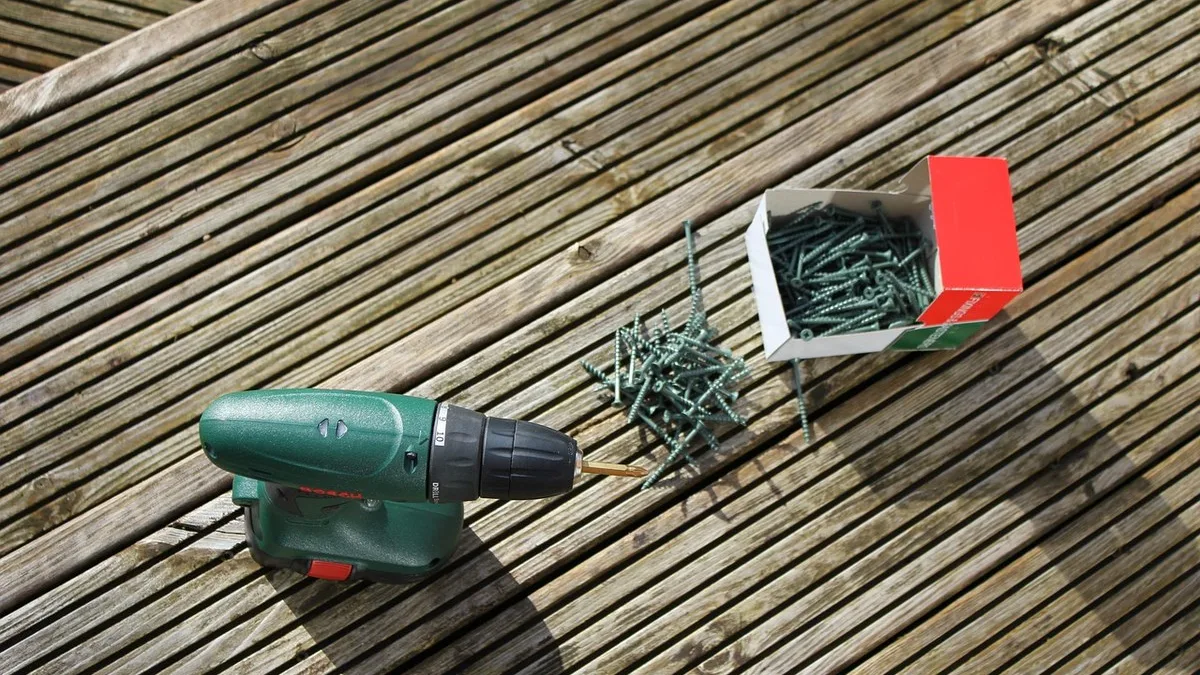 Cordless drill and a box of deck screws on a grooved composite deck