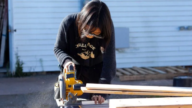 Person using a cordless circular saw to cut a board outdoors