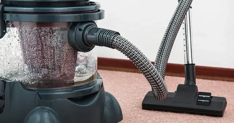 Canister vacuum cleaning carpet with a wood baseboard visible